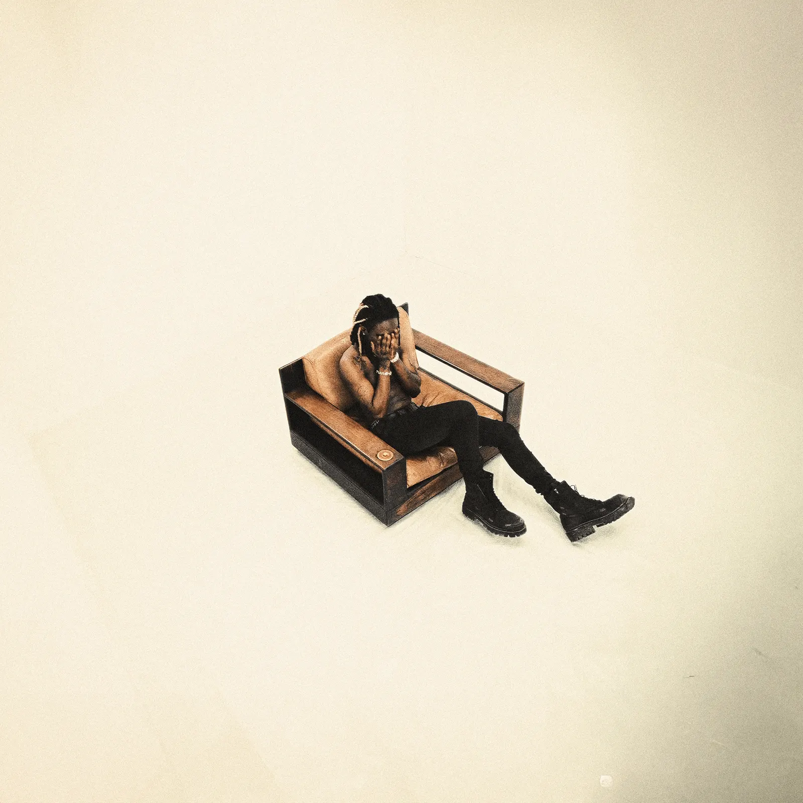 man covering face in wooden armchair, minimalist cream room, album art
